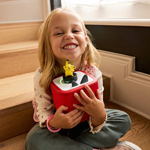 A girl is holding the toniebox, listening the Pikachu Tonie and smiling. 