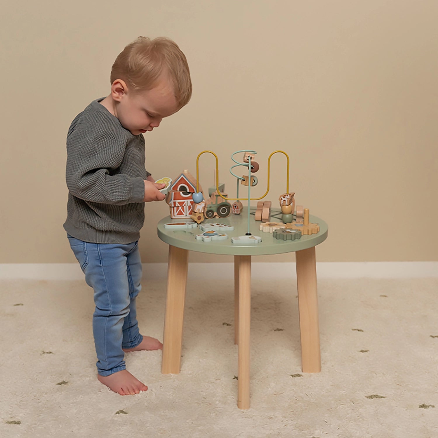 Toddler standing and playing at wooden activity table.