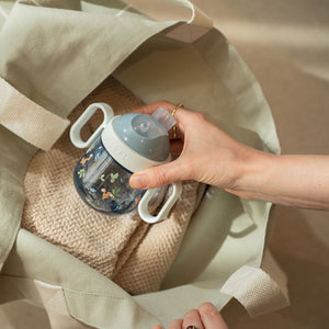 A person's hand placing the Little Dutch Forest Friends spout cup into a beige tote bag, demonstrating its leak-proof and portable design for travel.