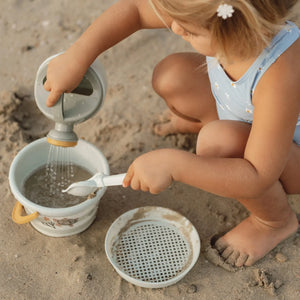 Toddler playing with green beach bucket and shovel by the seaside.