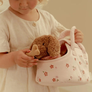 Child holding a plush toy and a floral-patterned bag against a plain background