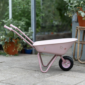Decorative children’s wheelbarrow in a gentle pink shade, styled with floral and fairy-inspired details for imaginative outdoor play