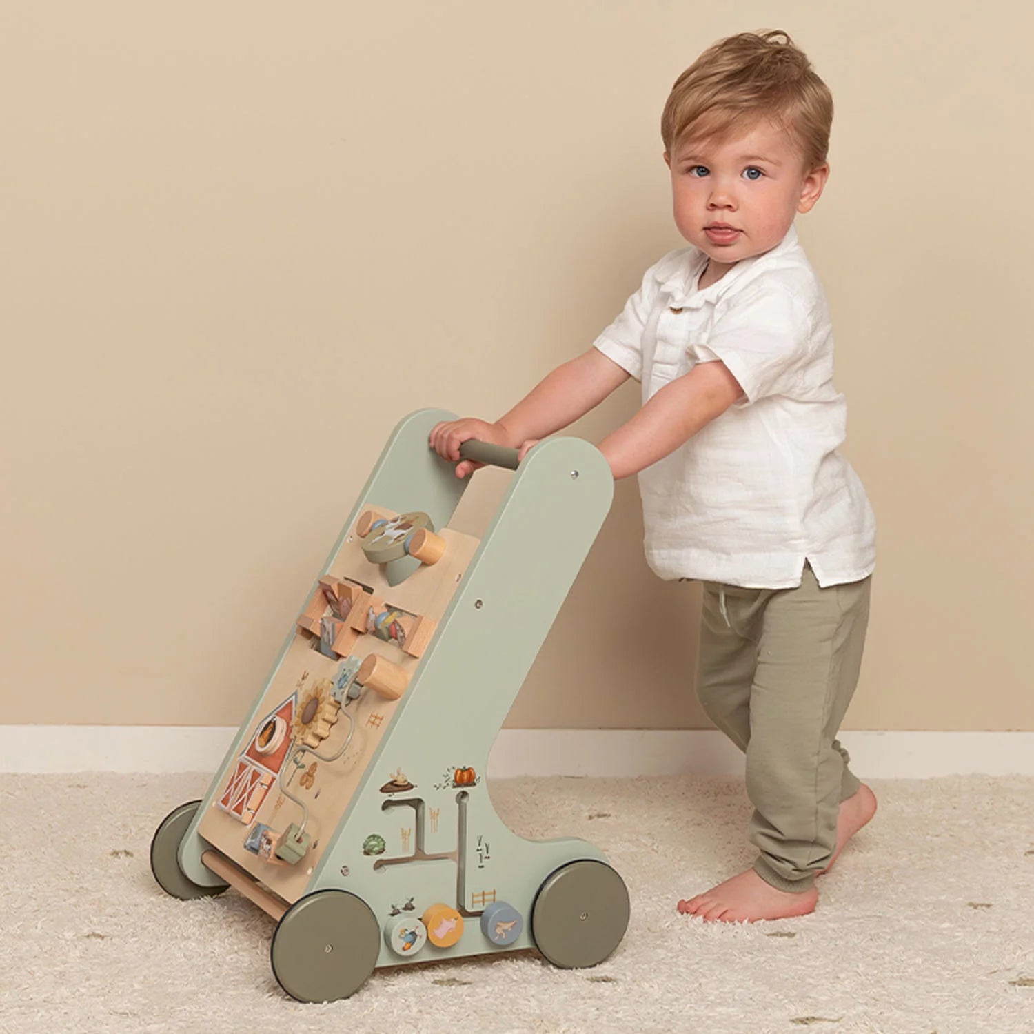 Toddler holding the handle of the Little Dutch wooden walker and pushing it across the floor.