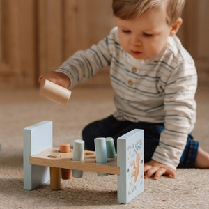 A baby boy is playing with the hammer bench.