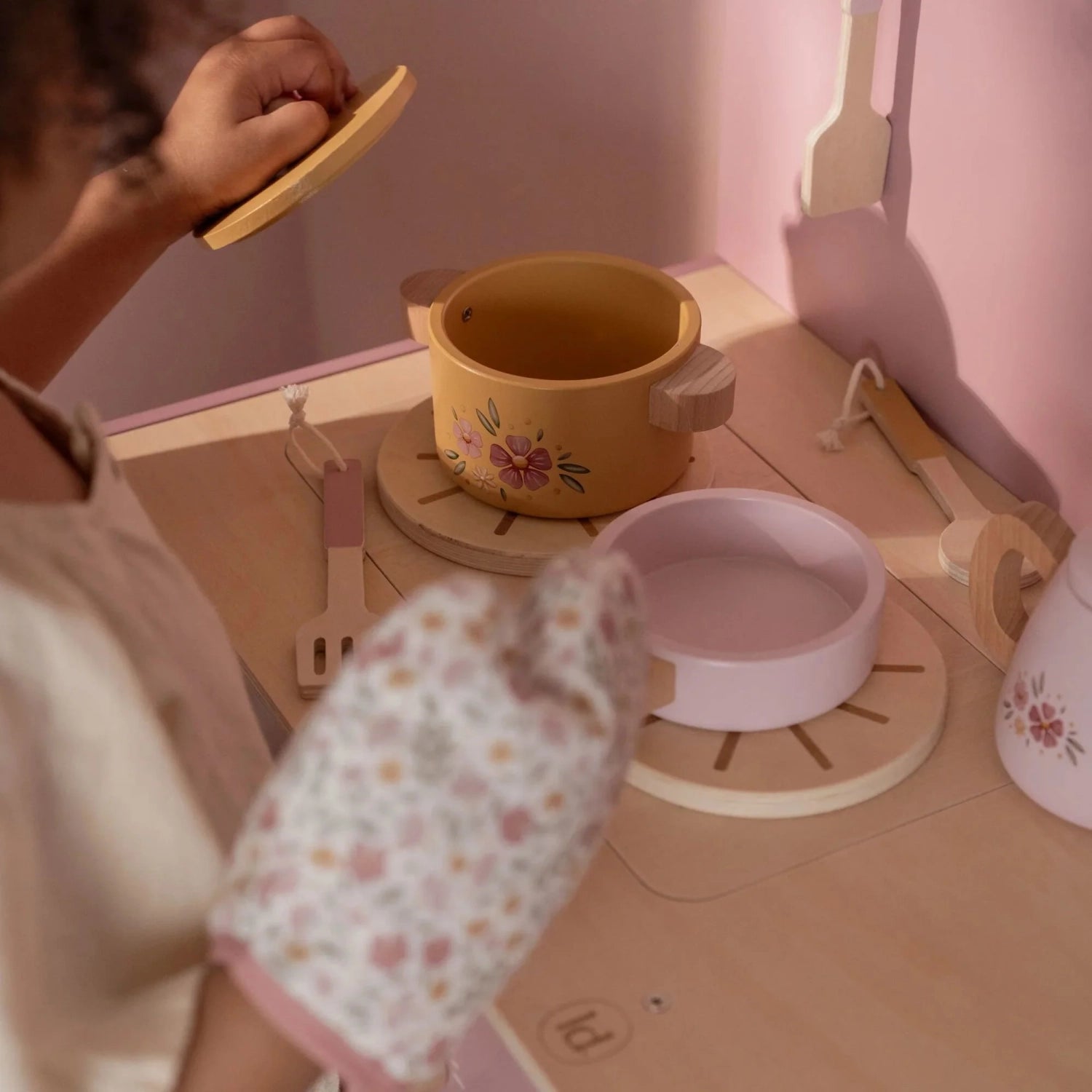 Pink toy kitchen stovetop with pans and utensils.