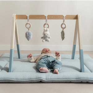 Happy baby playing under the Miffy baby gym with toys in reach.