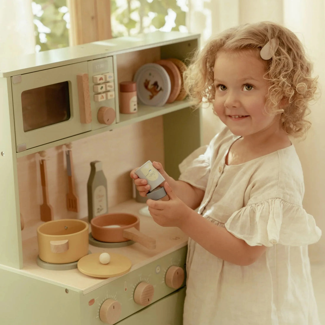 Child playing with a mint toy kitchen set in a bright room.