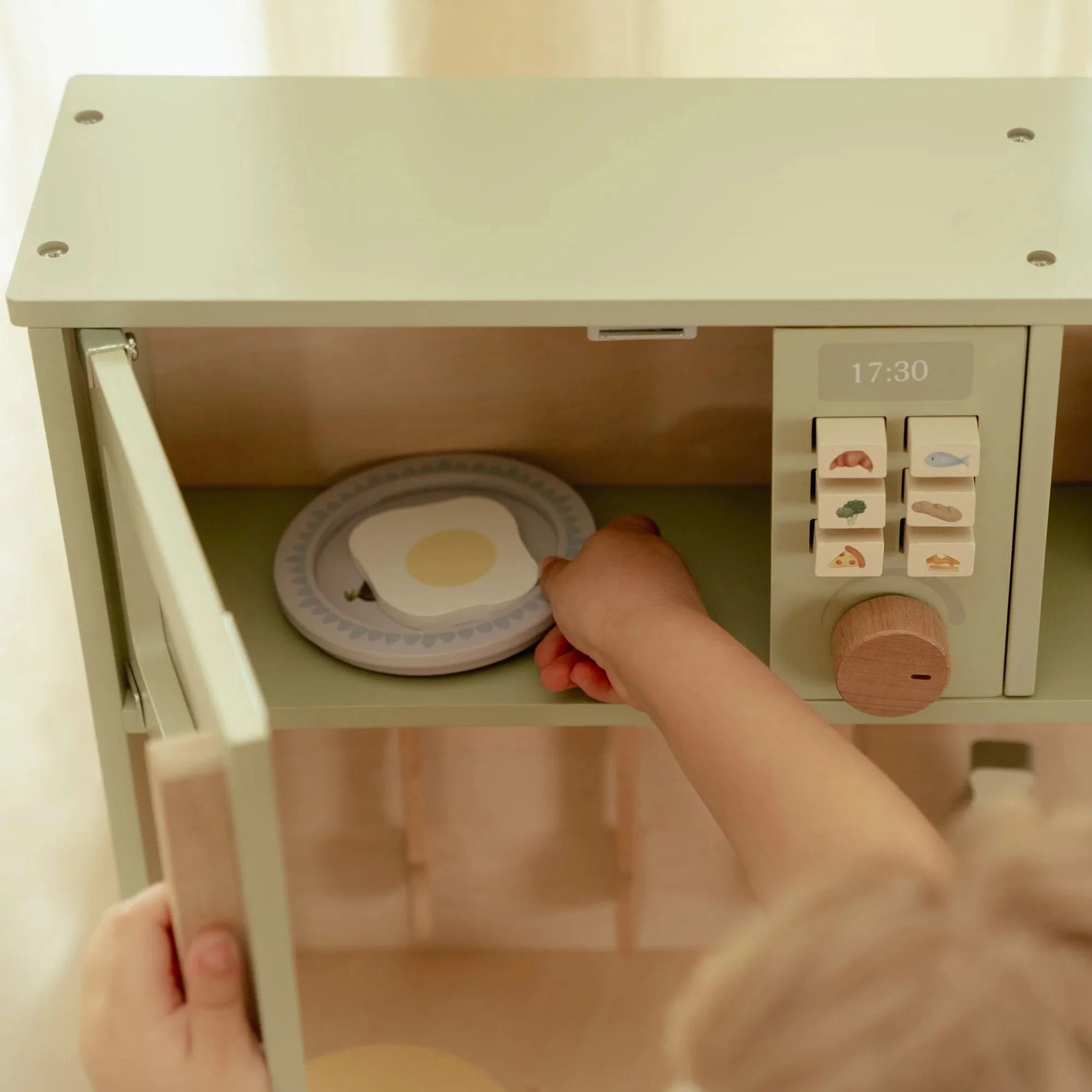 Child playing with a toy microwave oven and plate set.