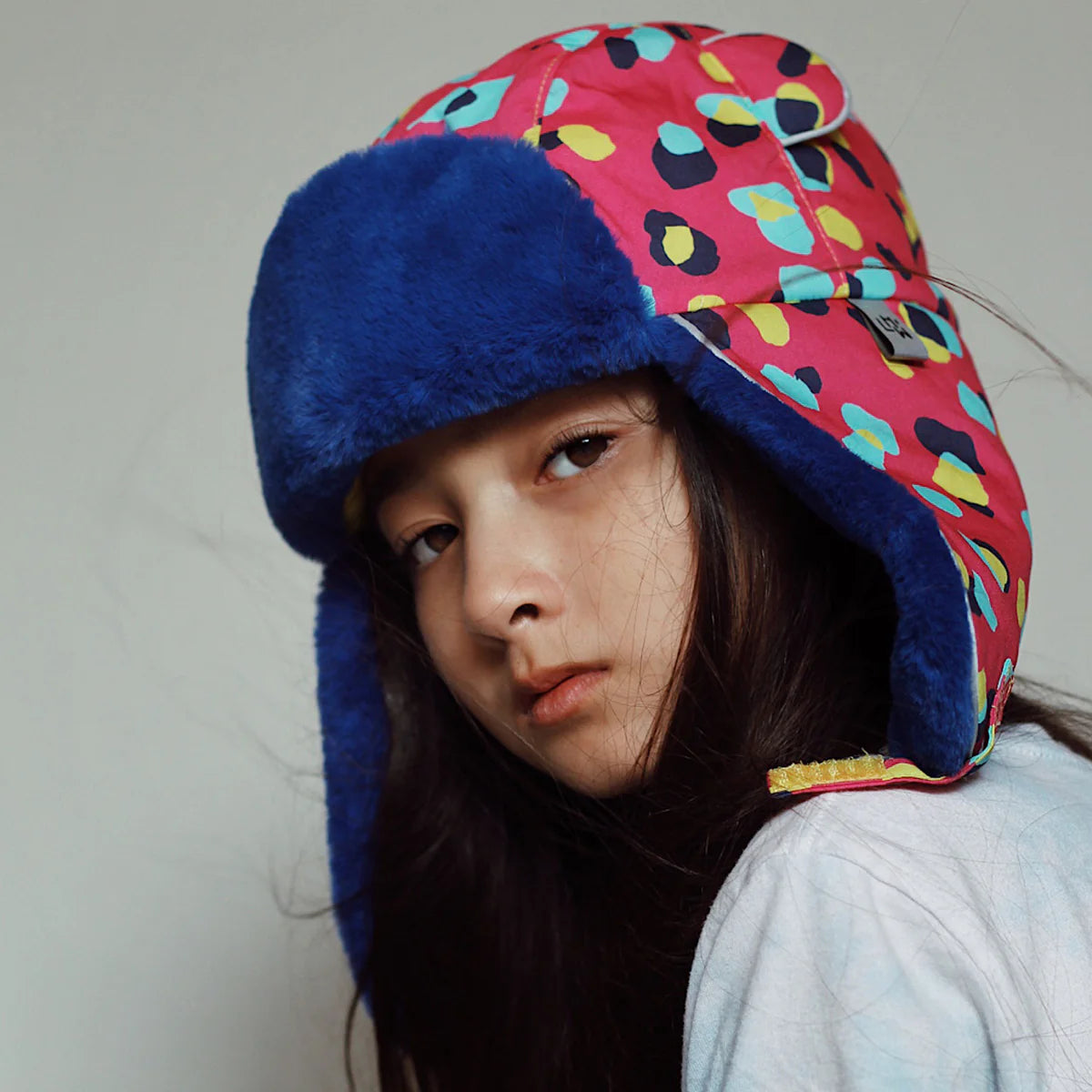 Person wearing a colorful patterned hat with blue fur trim on a plain background