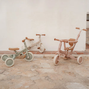Two Little Dutch 4-in-1 Tricycles, one in pink and one in green, displayed side-by-side indoors as classic tricycles
