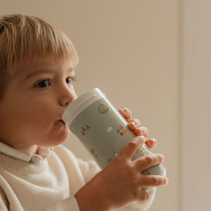 Profile view of a young child drinking from the light green Little Farm school beaker.