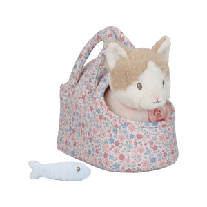 The plush beige and white cat, Marley, sitting inside the pink and blue floral print carry bag, with the light blue toy fish resting on the ground in front of it.
