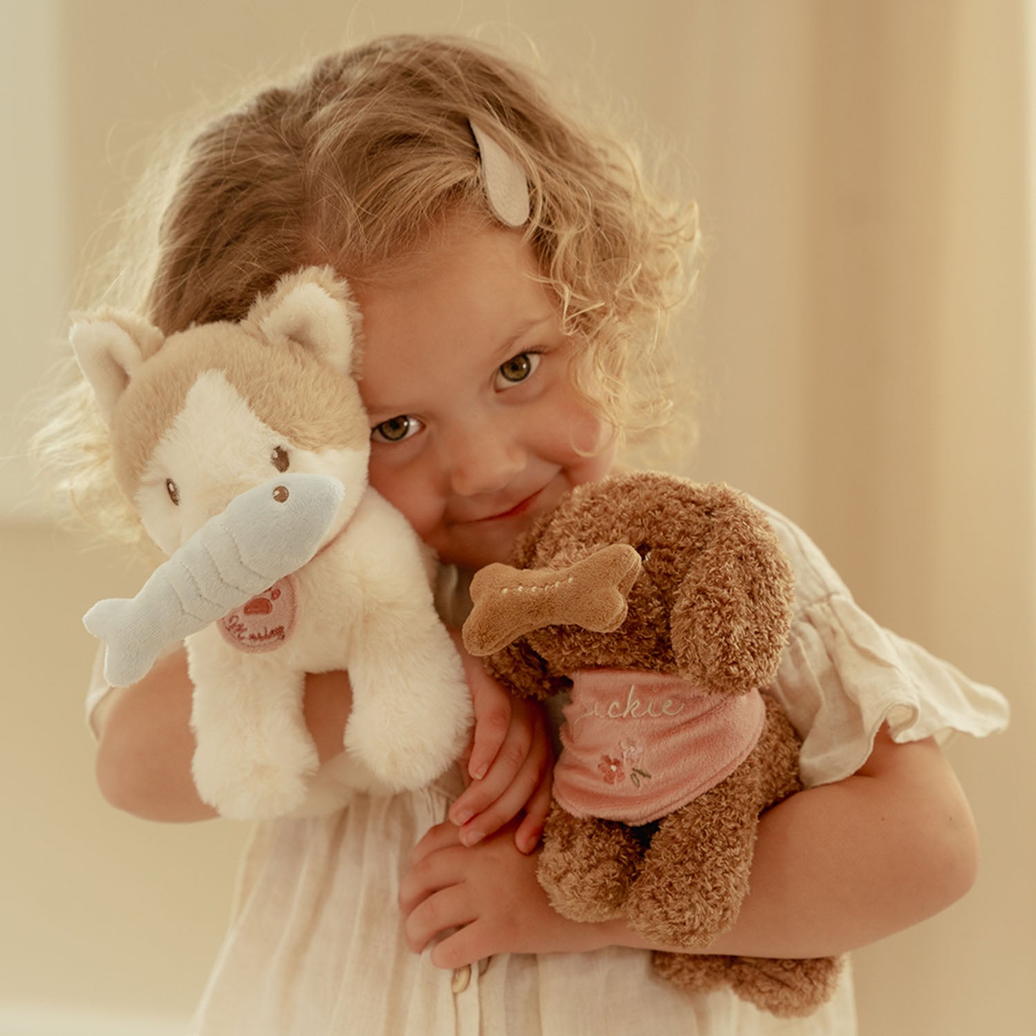 A smiling young girl holding and cuddling the plush cat alongside another brown plush toy.