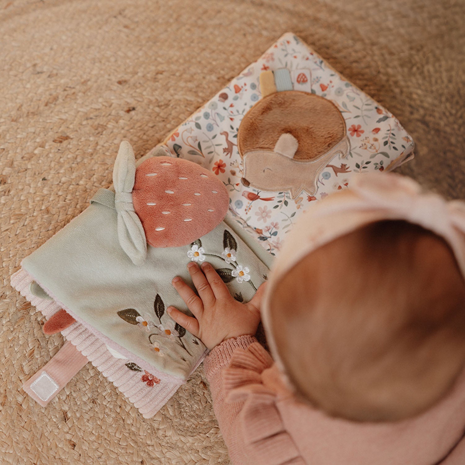 Baby interacting with a soft book and plush toy on a carpeted floor