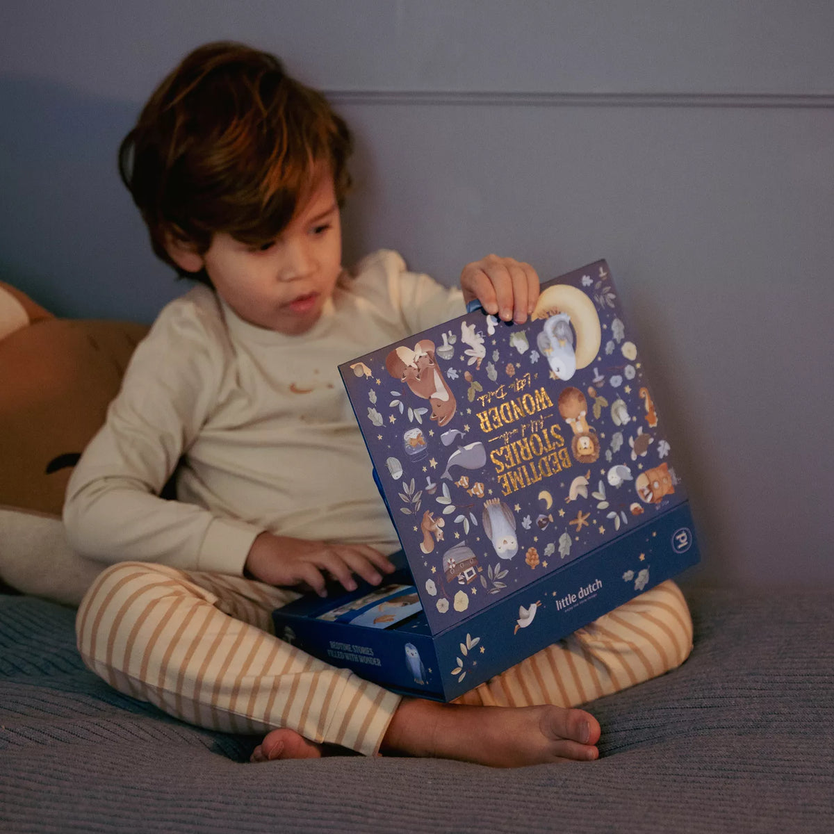 Child opening Little Dutch story projector box with illustrations on a bed