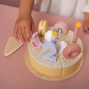 Close-up of a child's hands using the wooden server to take a slice of the pink Little Dutch birthday cake.