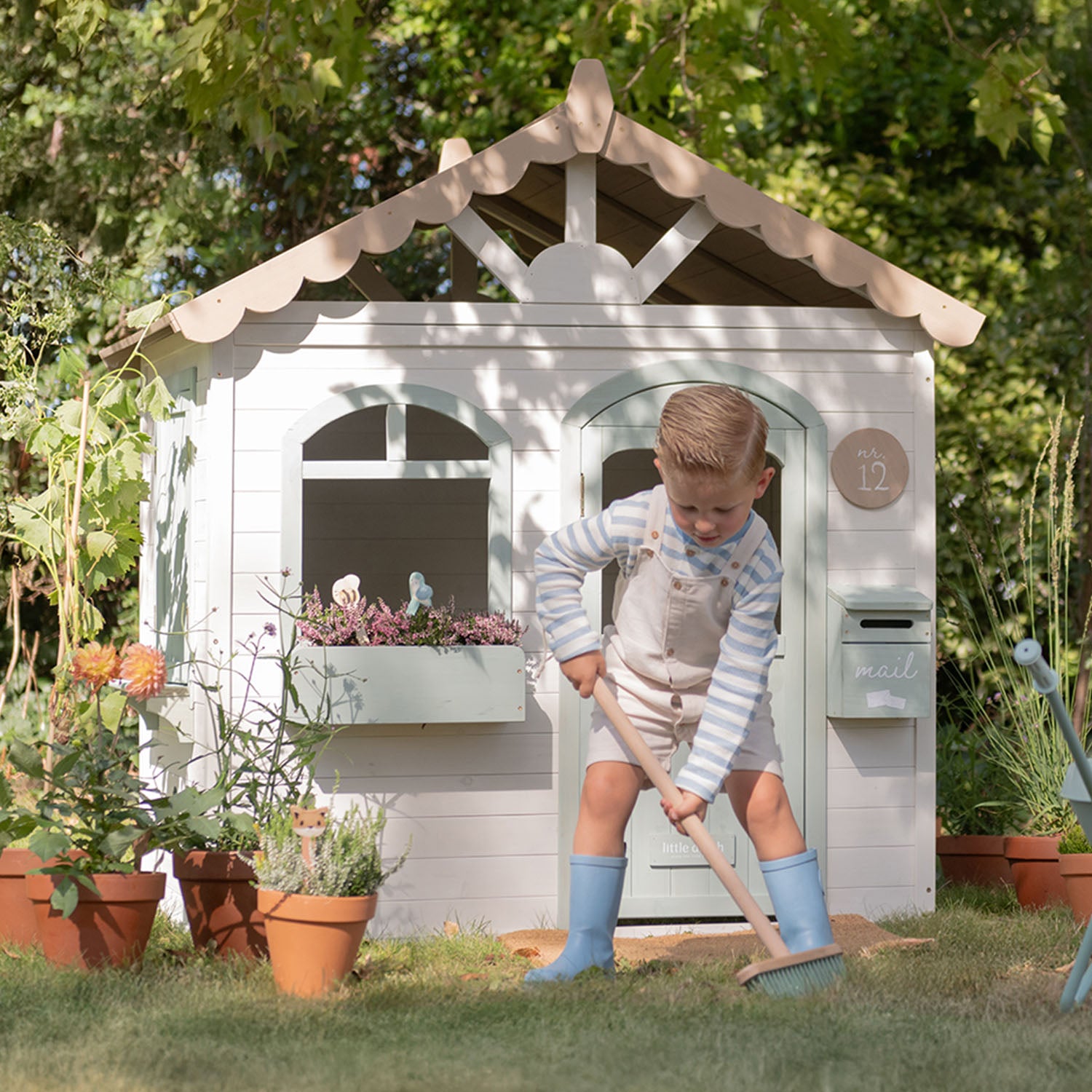 A child is pretend working in the garden in front of the little ducth wooden garden playhouse.