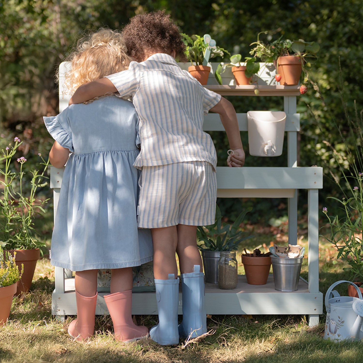Two young children standing together playing with the Little Dutch wooden mud kitchen in an outdoor garden setting
