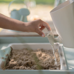Close-up of a child using the working water tap and reservoir to pour water into a basin filled with sand.