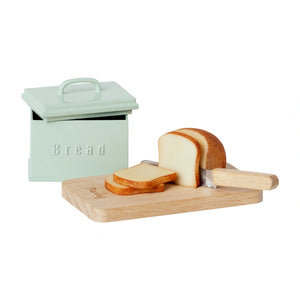 A miniature mint green bread box with utensils including a half loaf of bread, three bread slices, a wooden cutting board, and a knife designed for dollhouse play.
