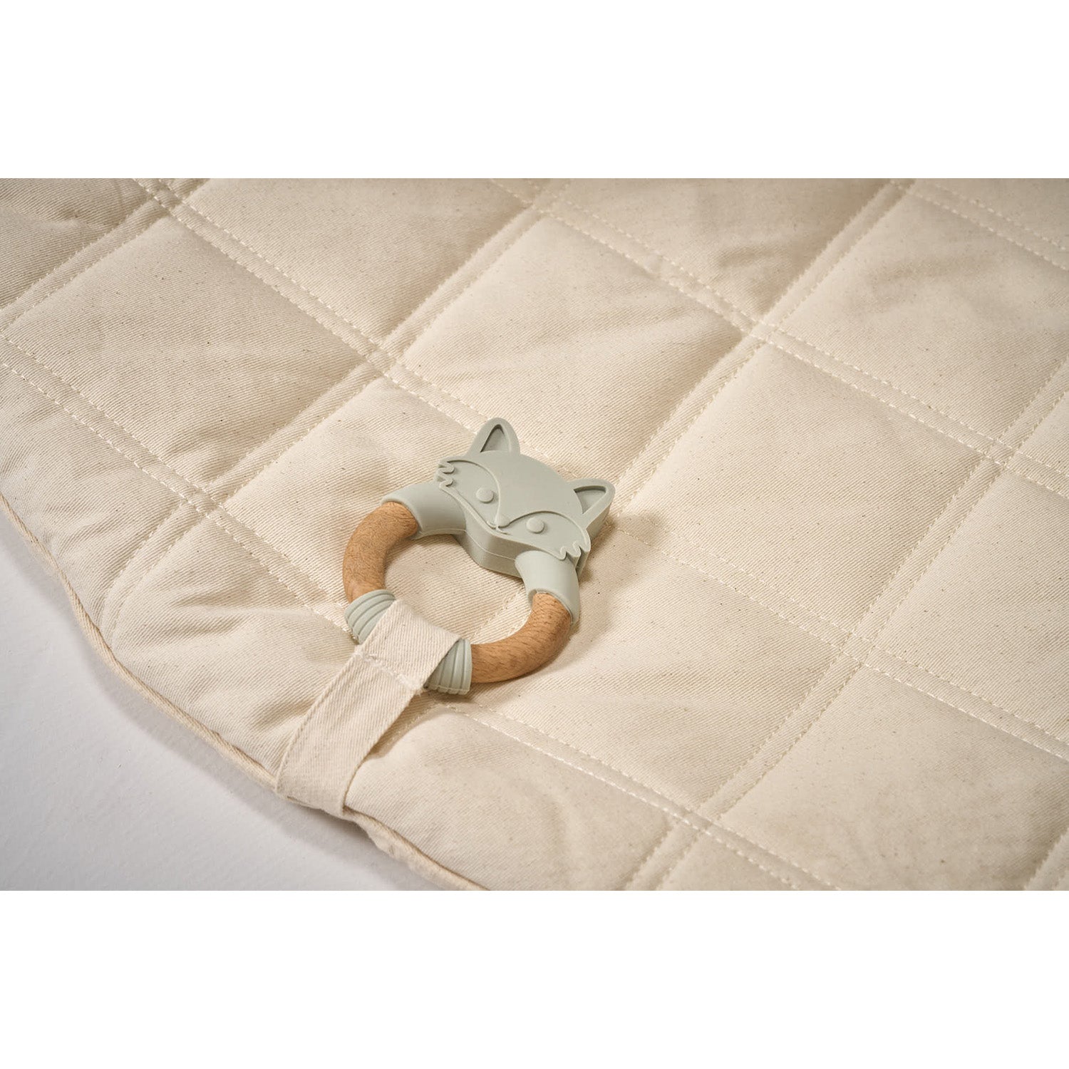 Teething ring with wooden handle and silicone fox design on a quilted fabric background