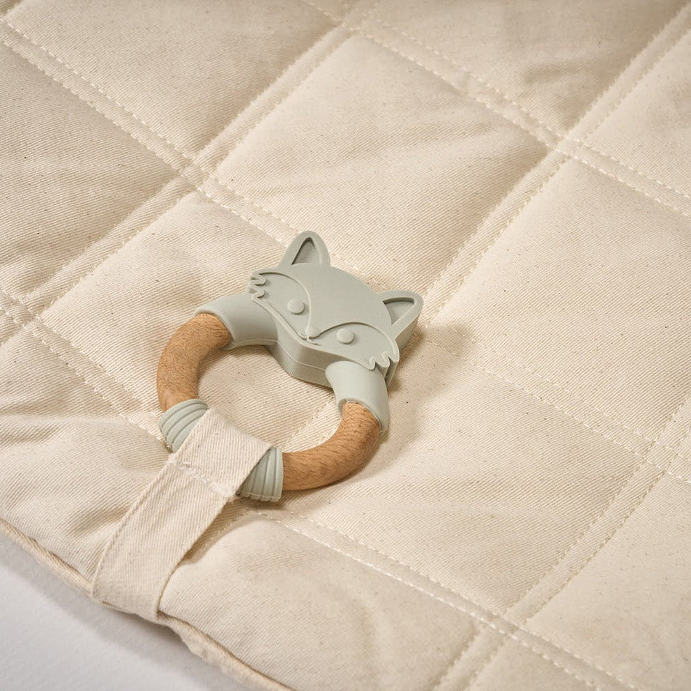 Teething ring with wooden handle and silicone fox design on a quilted fabric background