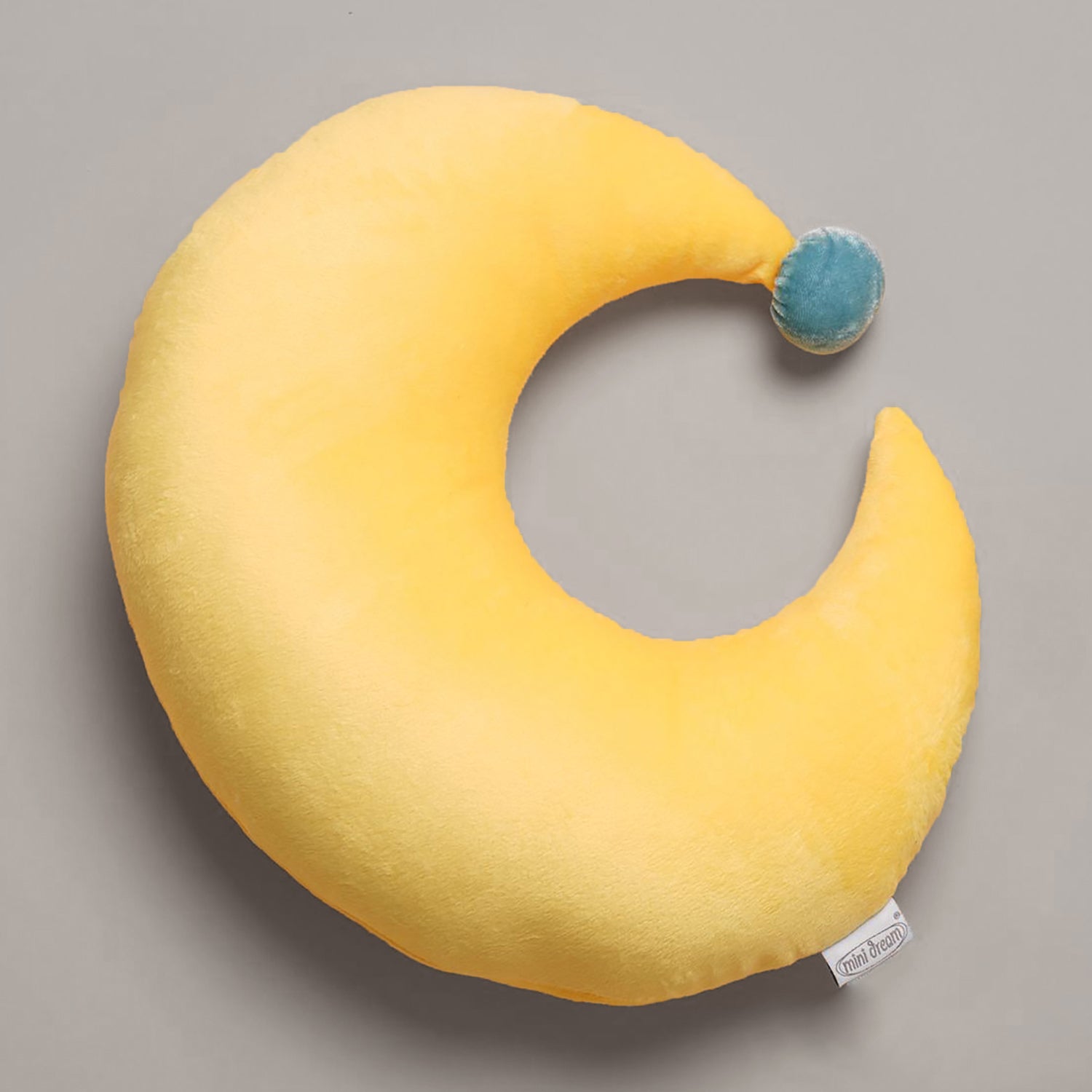 Yellow crescent moon-shaped pillow with a blue pom-pom on a gray background