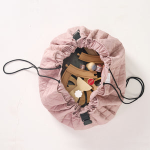 Pink playmat partially cinched together into a bag, revealing wooden blocks inside.