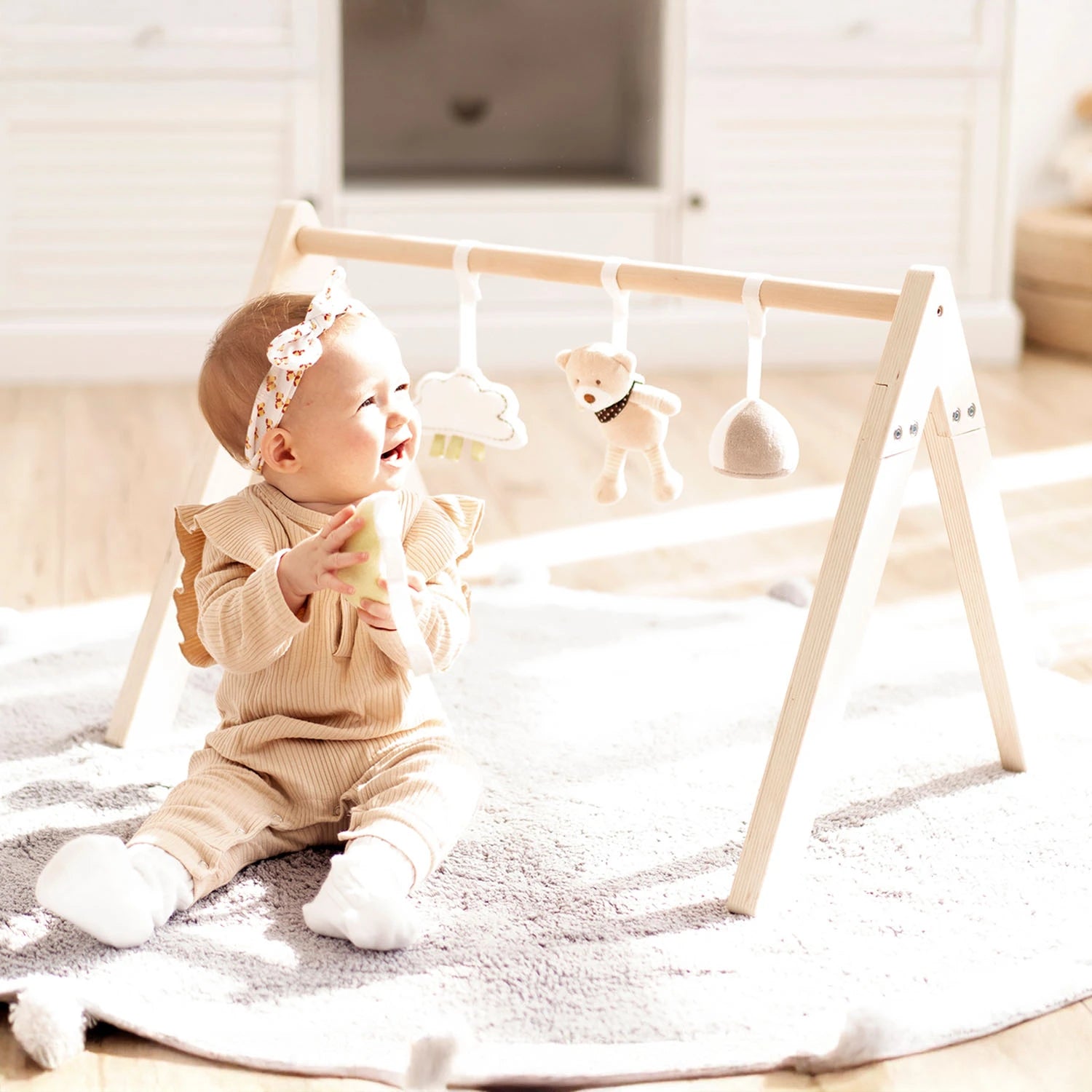 Happy baby playing with baby gym frame hanging toys.