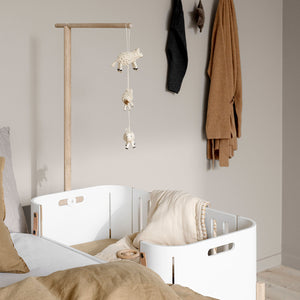 Functional wooden holder designed for baby sleep and comfort setup. Adjustable co-sleeper including bench conversion height feature shown next to a standard bed frame