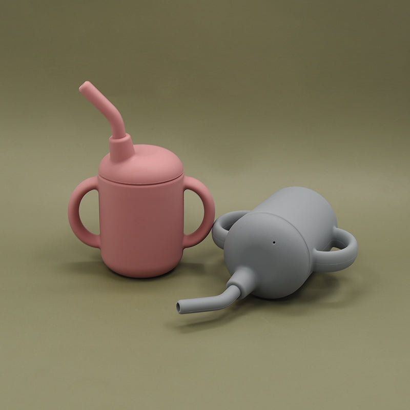 Blush pink and grey-blue silicone sippy cups placed together on a dark sage background.