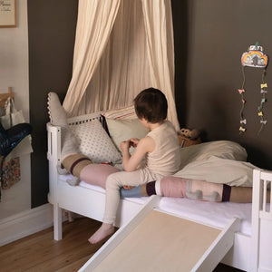 Child sitting on converted Sebra Junior & Grow bed with lowered side rail, showing junior bed configuration