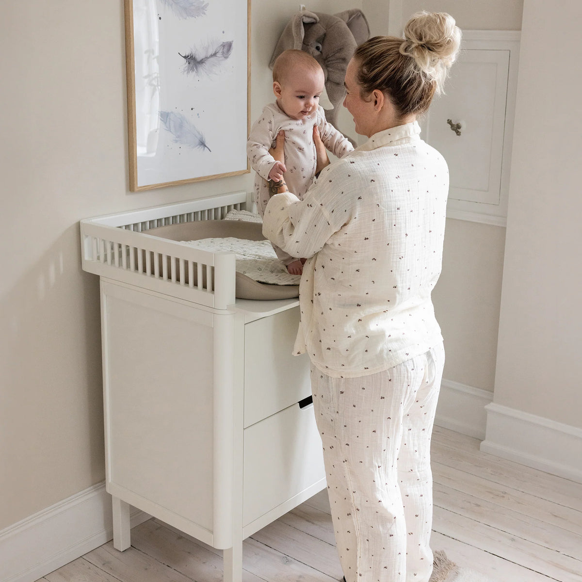 Parent standing at white Sebra changing unit changing a baby in bright nursery