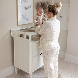 Parent standing at white Sebra changing unit changing a baby in bright nursery