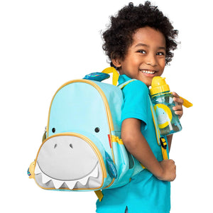 A toddler wearing a Skip Hop Zoo Toddler Backpack in the Bee design, standing in a park.
