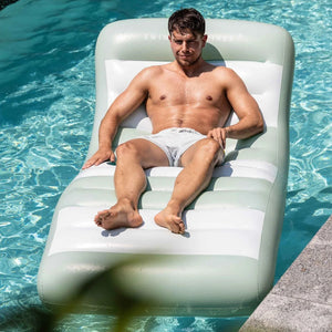 An adult man is sunbathing on the beach lying on the floating lounge.