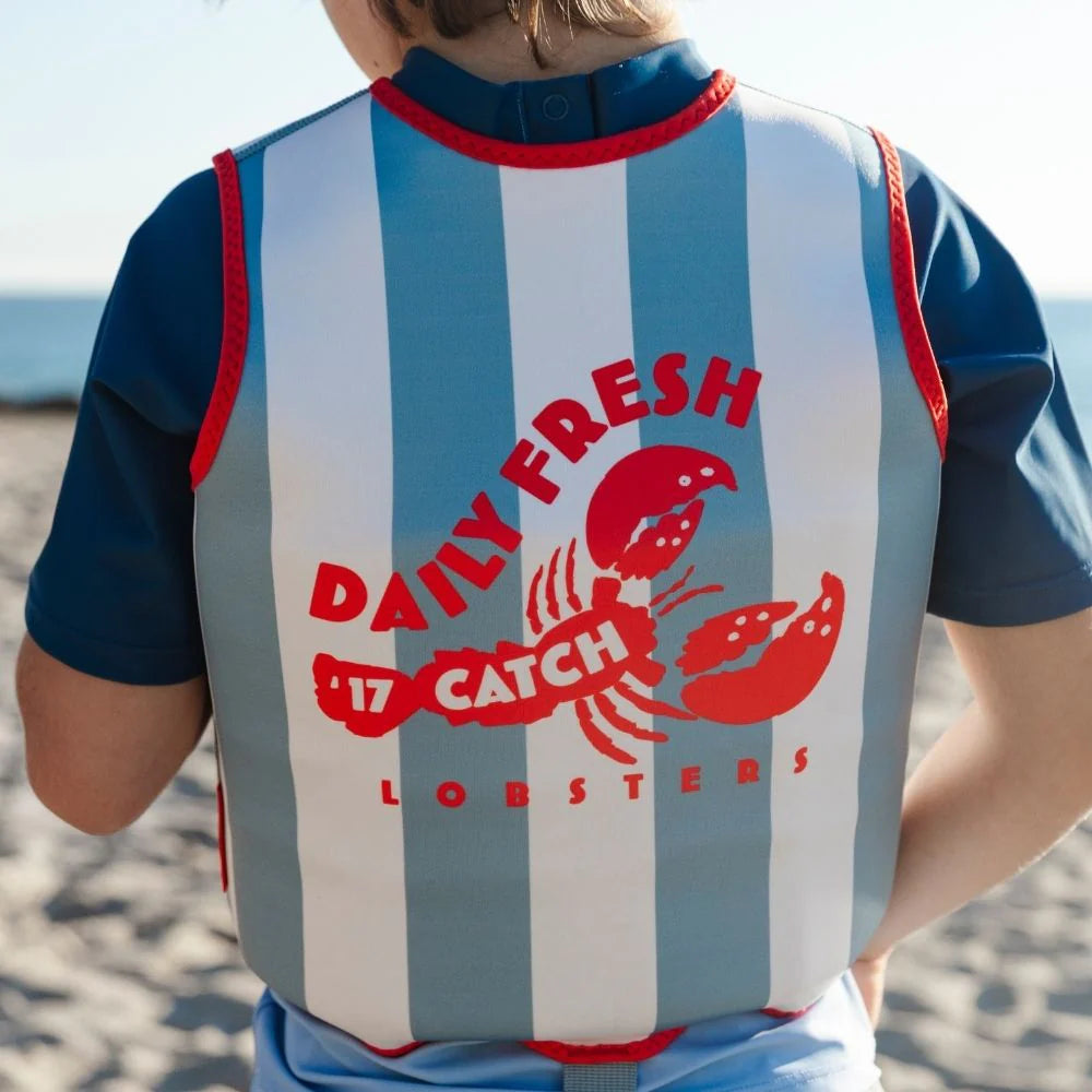 A young child wearing the "Catch of the Day" swim vest while playing safely in a beach.