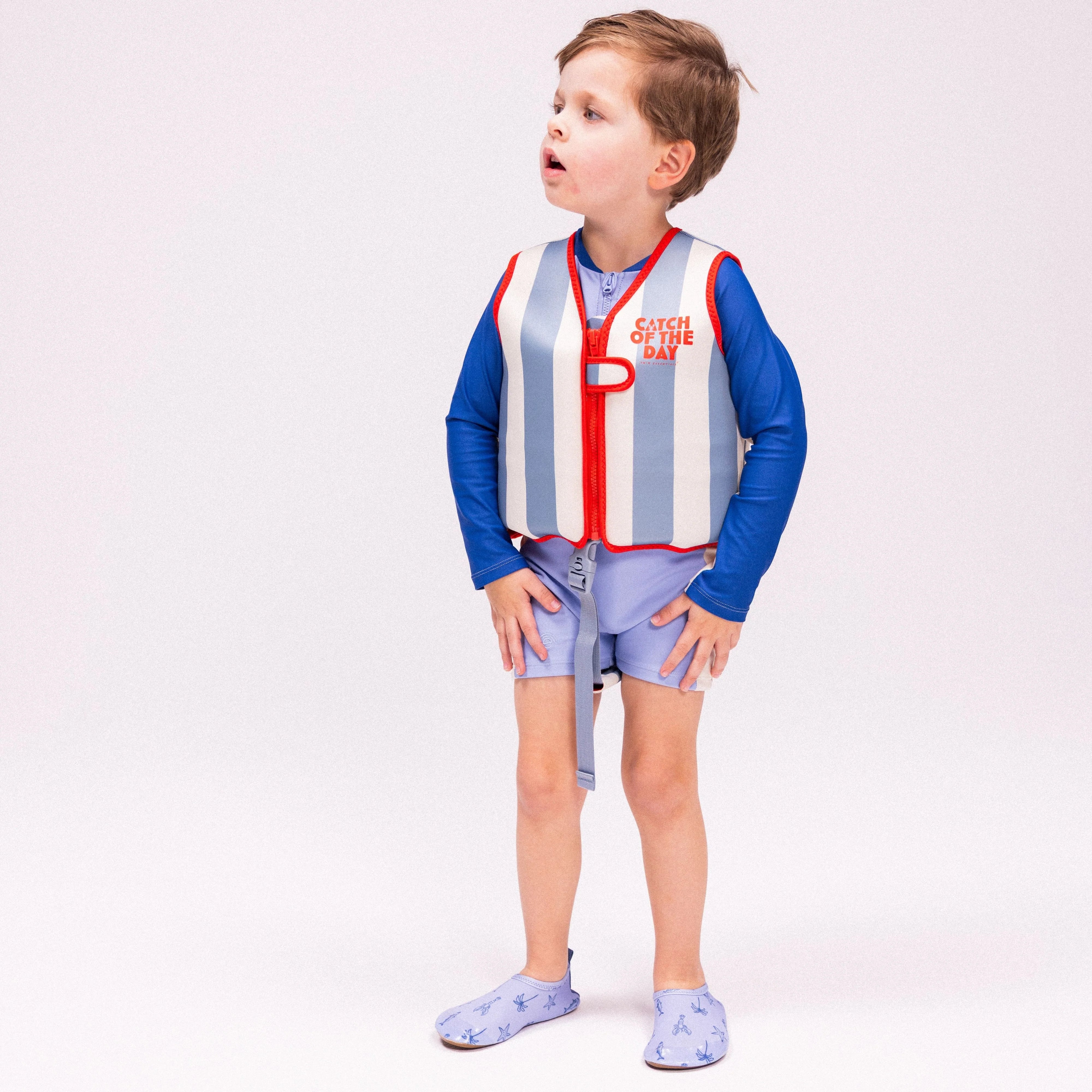 A boy is standing wearing the swim essentials swim vest in red and blue colour.