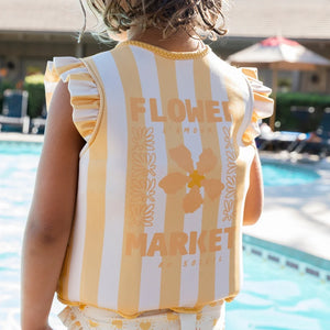 A young child wearing the floral swim vest while smiling and playing in a sunny pool.