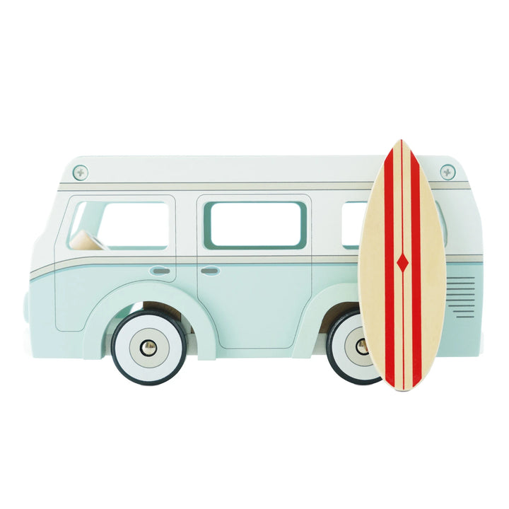 A blue and white wooden toy van with a red surfboard strapped to the roof. The van has cream colored wheels and windows. It is parked on a white background