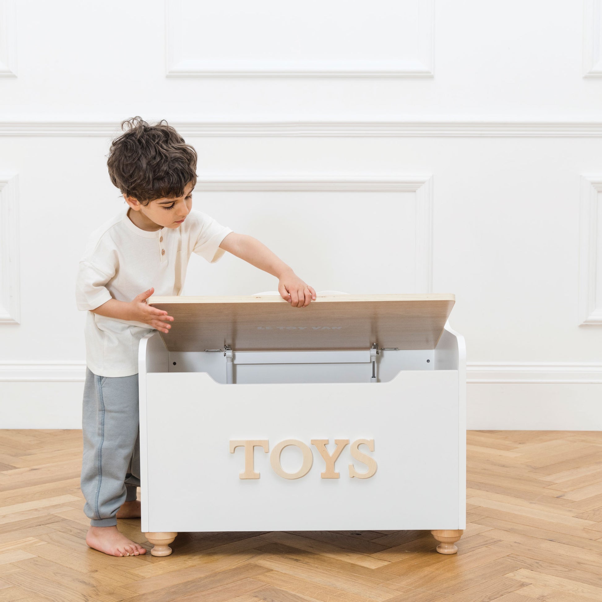 Child opening a toy storage box with 'TOYS' on it in a room.