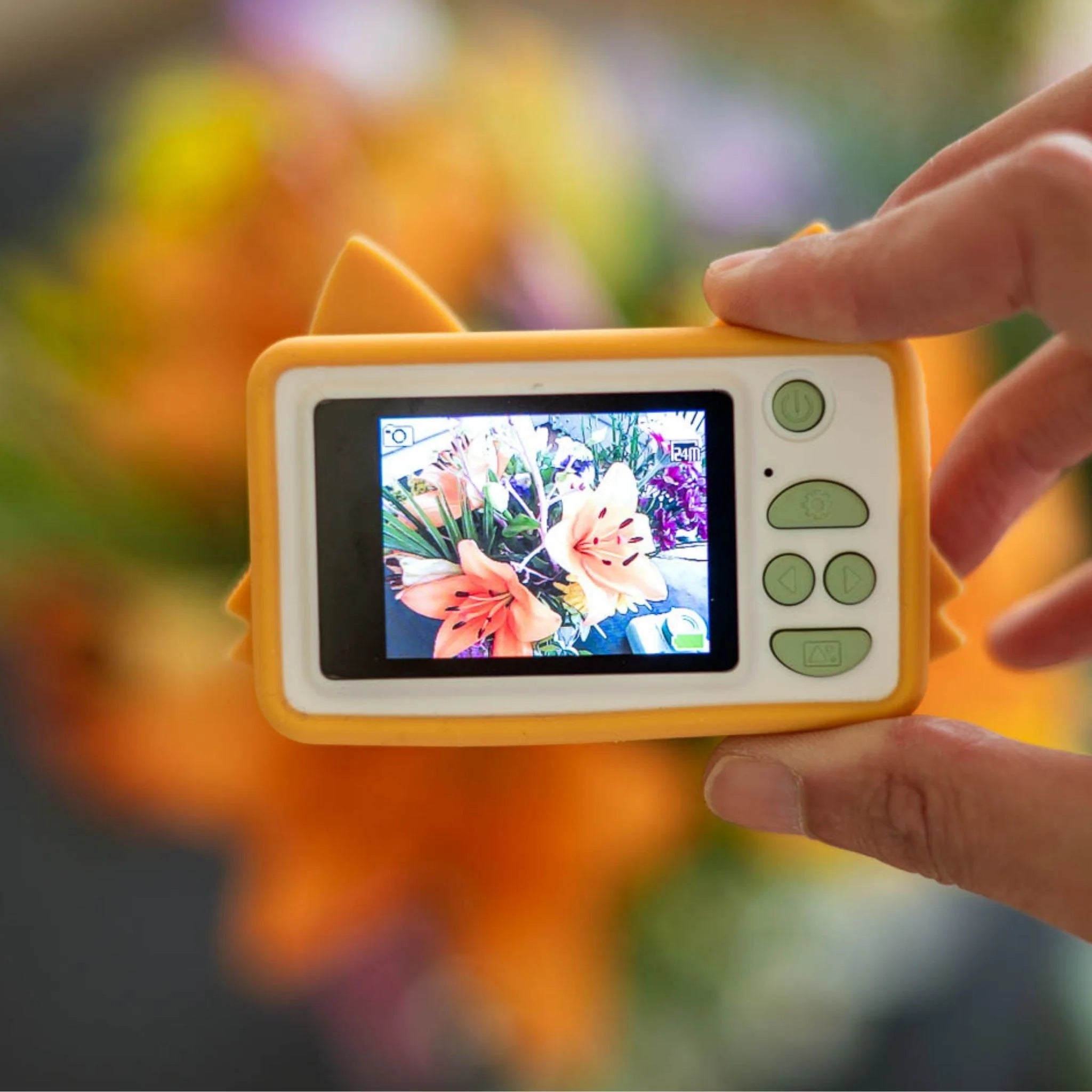 Hand holding a small digital camera with a screen displaying a floral arrangement.