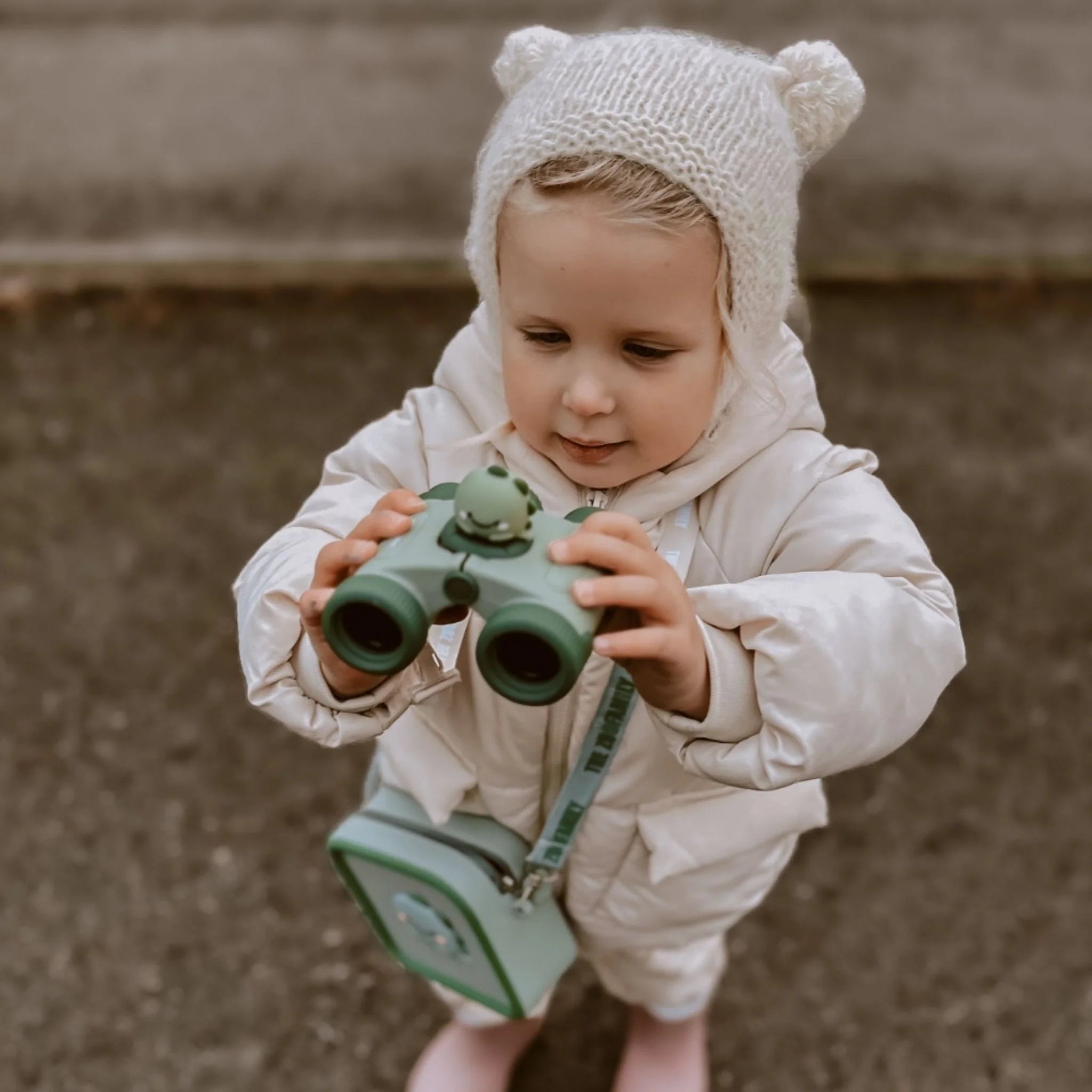 Girl holding green zoo eyes binoculars in both hands.