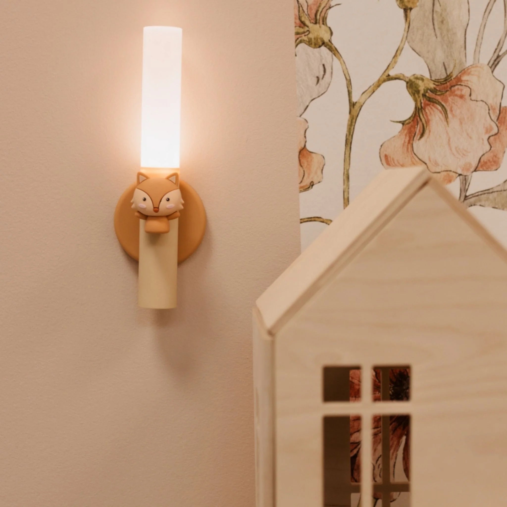 Wall-mounted light fixture with fox design on a wall with floral wallpaper.