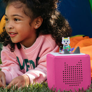 A smiling young child sitting comfortably and listening intently to audio stories playing from a Toniebox with the PAW Patrol Everest figure placed on top.