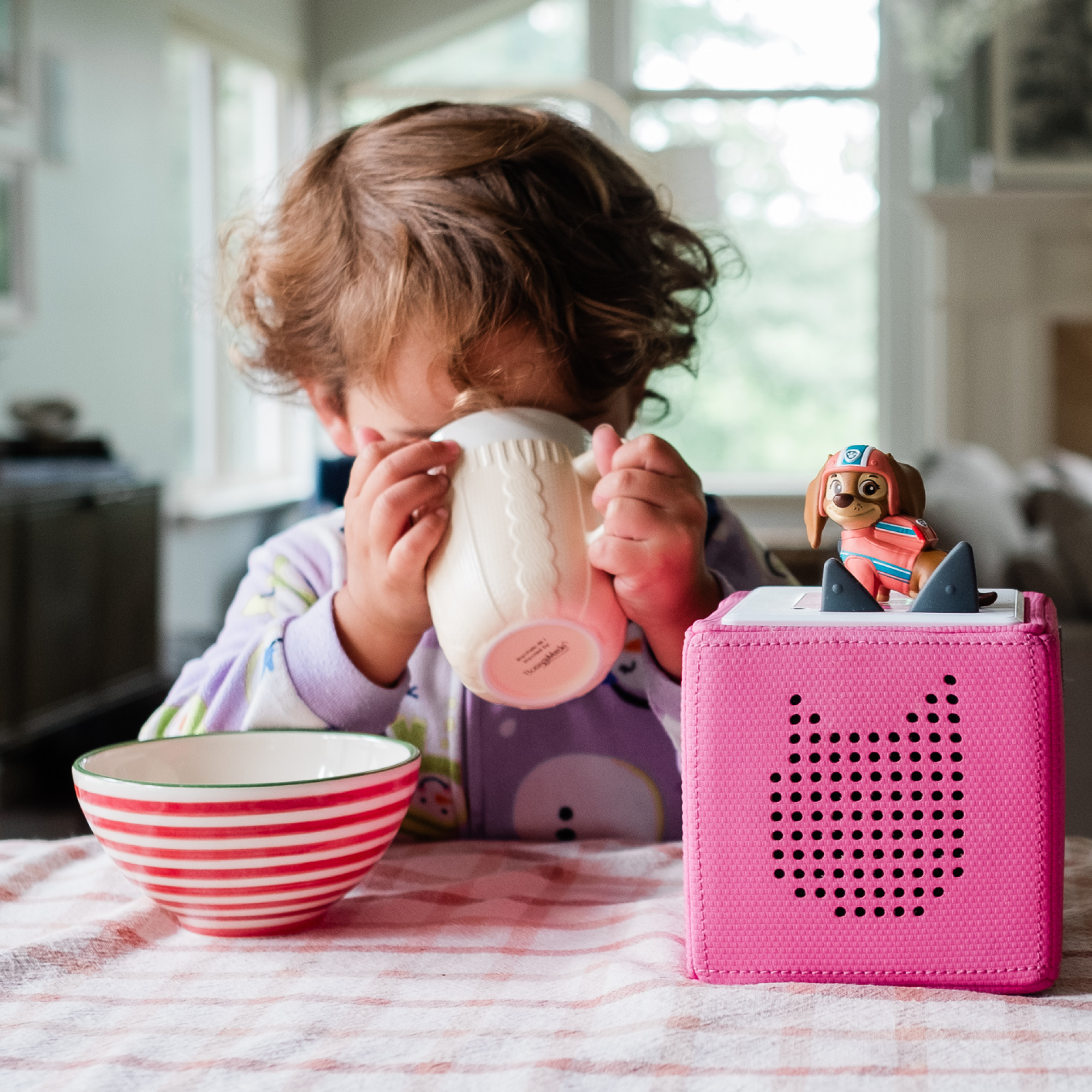 A happy child having food and listening to stories coming from the Liberty Tonie on a pink Toniebox.