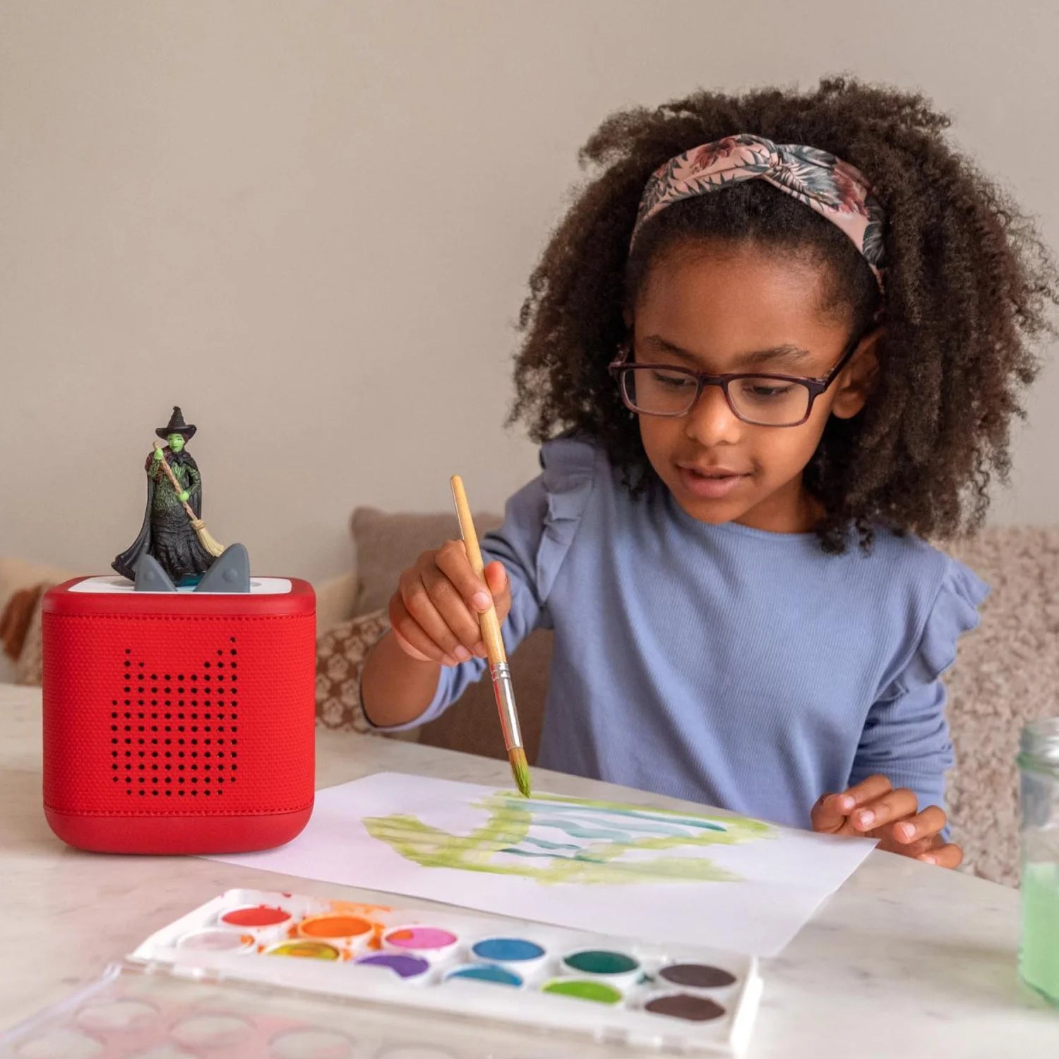 A girl is listening to the wicked tonie, and drawing a painting.