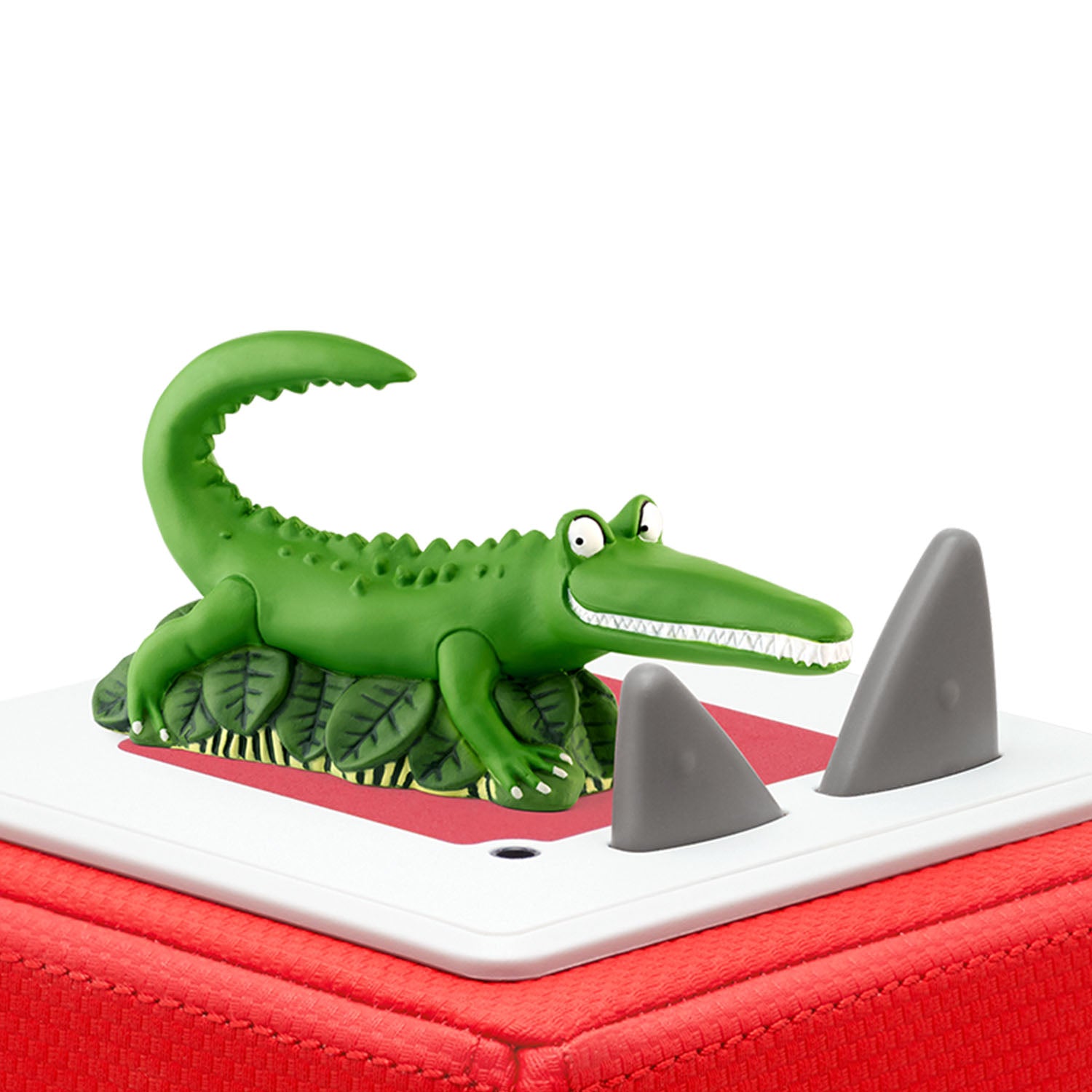 A close-up view of the green crocodile Tonie figurine sitting securely on top of a red and white Toniebox speaker.