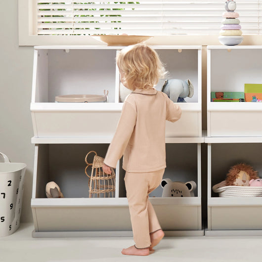 Child putting toys away in a white and grey wooden storage trunk.