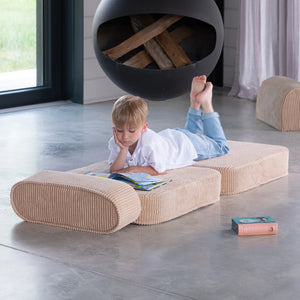 A boy is reading a book lying on the Wigiwama foldable chair.